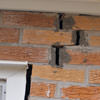 A brick wall displaying stair-step cracks and messy tuckpointing on a Provo home